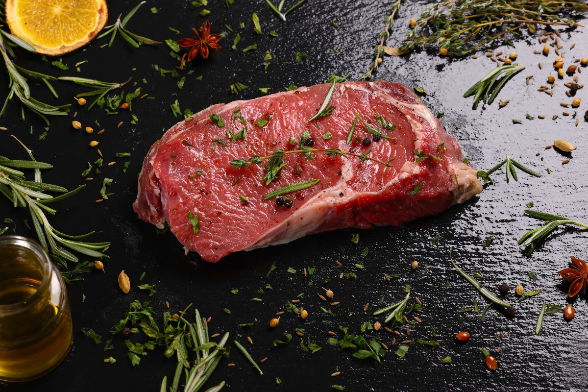 Cooked chuck steak sliced thinly on a cutting board with fresh herbs