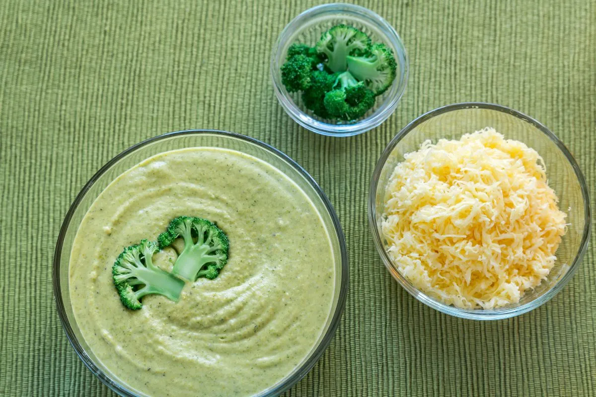A steaming bowl of broccoli cheese soup served with a crusty baguette