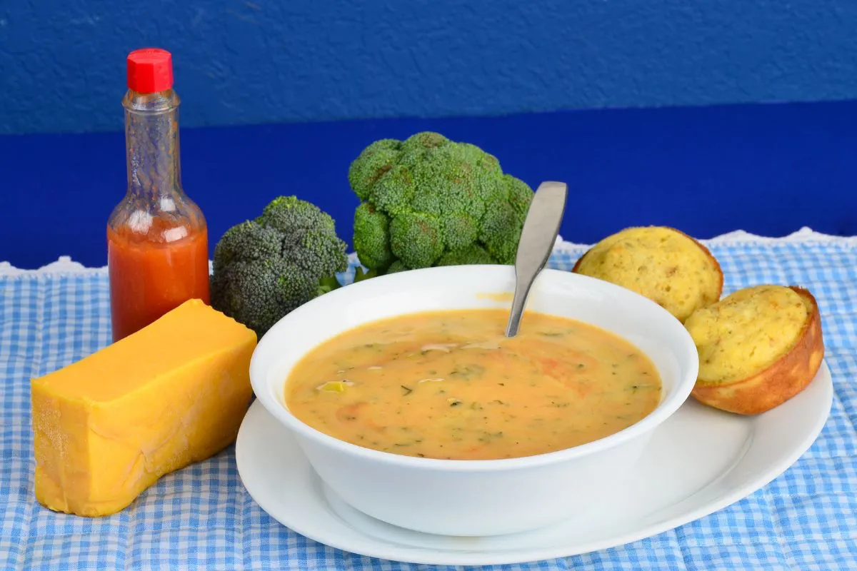 A steaming bowl of broccoli cheese soup served with a crusty baguette