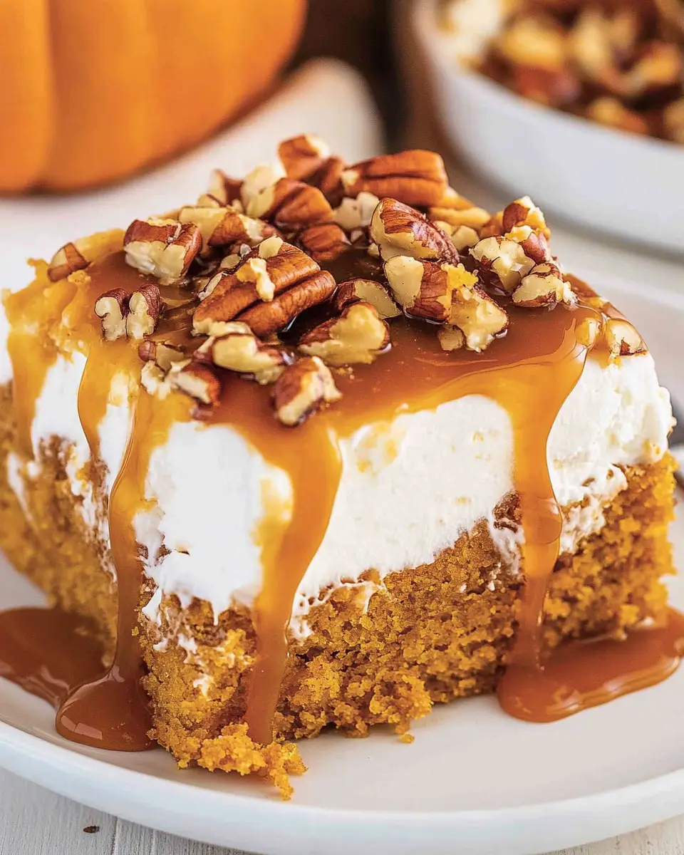 A close-up shot of a single slice of pumpkin caramel poke cake on a white plate, showing the distinct layers of cake, caramel, and whipped topping.